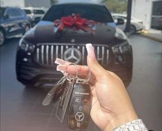 a hand holding keys in front of a car with a red bow on the hood