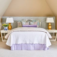 a white bed sitting under two lamps in a bedroom next to a table with flowers on it