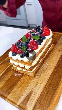 a person standing over a wooden cutting board with a piece of cake on top of it