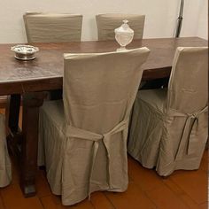 a dining room table with chairs covered in beige cloths and a vase on top