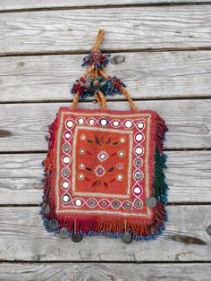 a small red bag hanging from a wooden wall with beads and fringes on it