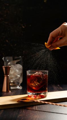 a person sprinkles sugar on top of a drink in a glass with an orange peel