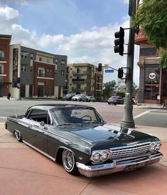 an old car is parked on the side of the road in front of a traffic light