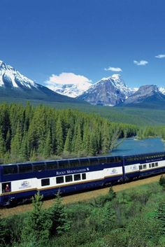 a passenger train traveling through the mountains with snow capped peaks in the background and trees on either side