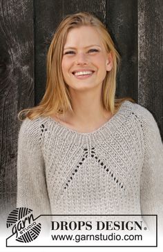 a woman wearing a white sweater standing in front of a wooden fence with the words drops design on it