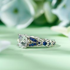 a diamond and blue sapphire ring sitting on top of a green surface with flowers in the background