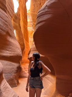 a woman standing in the middle of a narrow slot between two large rock formations, with her hands on her hips