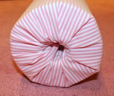 a pink and white striped vase sitting on top of a floor next to a wall