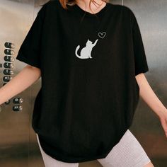 a woman wearing a black shirt with a white cat on it's left chest