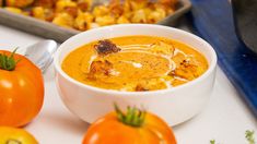 a white bowl filled with soup next to some tomatoes and other food on a table