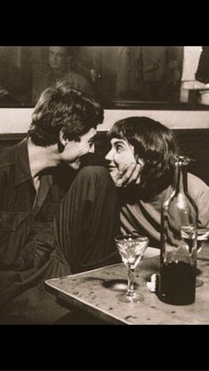 two young men sitting at a table with drinks in front of them, one is talking to the other