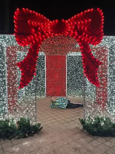 a large red bow on top of a metal pole next to a wall covered in christmas lights