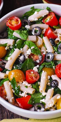 a white bowl filled with pasta salad on top of a wooden table next to a yellow napkin