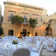 tables and chairs are set up in front of an old building with white linens