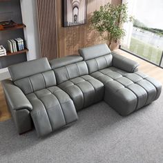 a grey leather sectional sofa sitting on top of a carpeted floor next to a window