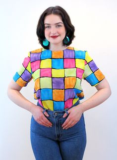 "This is a sweet colorful 90s vintage \"Notations\" top! It's a bright color block geometric square print in shades of pink, blue, yellow, purple and orange with black grid lines. A short sleeved pullover, it has a boxy shape, a high round neckline, no shoulder pads, and it closes with a back keyhole neckline and a black button and loop. The fabric is a lightweight silken polyester. This top is in very good clean vintage condition, no flaws noted. The label says \"Notations, Size S, 100% Polyest Retro Multicolor Tops With Rainbow Print, Retro Multicolor Rainbow Print Top, Retro Plaid Top With Graphic Print, Retro Multicolor Tops With Vibrant Print, Retro Multicolor Top With Vibrant Print, Trendy Multicolor Retro Print Top, Trendy Multicolor Top With Retro Print, Multicolor Fun Tops With Retro Print, Multicolor Retro Print Fun Top