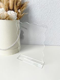 a white vase with some dried flowers in it next to a wire holder on a table