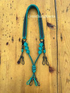 a turquoise colored rope with metal hooks on top of a wooden floor next to a pair of scissors