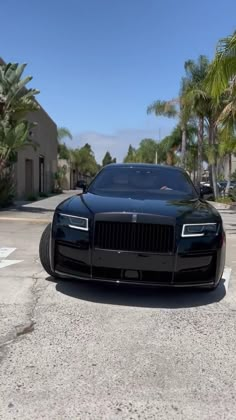 a black rolls royce parked in a parking lot with palm trees and buildings behind it