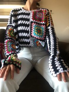 a woman sitting on top of a couch wearing white jeans and a crocheted jacket