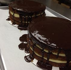 two cakes sitting on top of a counter covered in chocolate frosting and drizzle