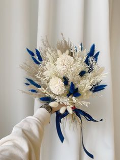 a bouquet of white and blue flowers is being held up by someone's hand