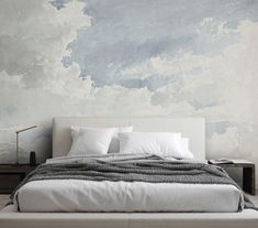 a bed with white linens and pillows in front of a painted sky wallpaper