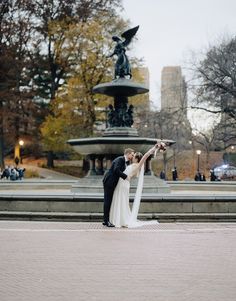 a bride and groom standing in front of a fountain holding each other's hands