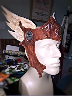 a white mannequin head wearing a wooden helmet with wings on it's head