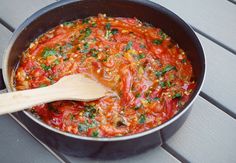 a wooden spoon is in a pot filled with tomato and basil sauce on a table