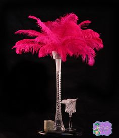 a tall glass vase with a pink feather tree in front of a black background,