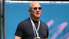 a bald man with sunglasses and a medal around his neck stands in front of a blue wall