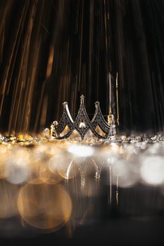 two tiaras sitting on top of a table next to each other with lights in the background