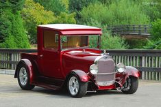 an old fashioned red car is parked on the side of the road with trees in the background