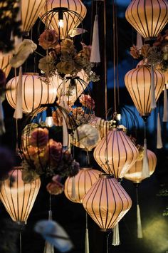 many lanterns are hanging from the ceiling and decorated with flowers, leaves and ribbons at night