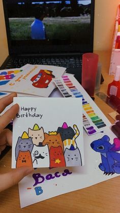 a person holding up a birthday card in front of a laptop