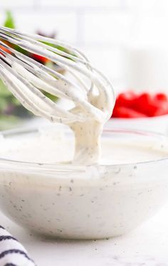 a whisk in a white bowl filled with cream cheese sauce on top of a counter