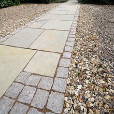 a stone walkway with gravel and bushes in the background