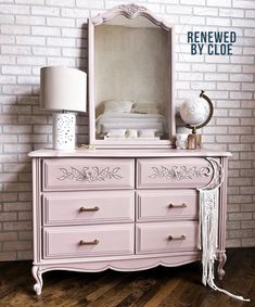 a pink dresser sitting next to a white brick wall with a mirror on top of it