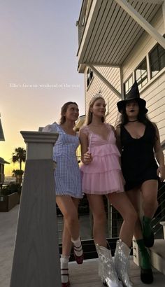 three women in short dresses and boots posing for the camera on a porch at sunset