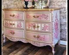 an ornate dresser with pink and white flowers on the top, in front of a brick wall