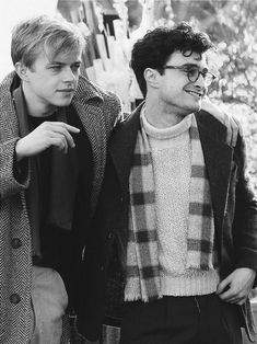 two young men standing next to each other in front of a tree and one is wearing a scarf