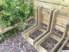 three wooden benches sitting next to each other on top of gravel covered ground with plants in the background