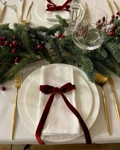 the table is set with white plates, silverware and greenery for christmas dinner