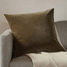 a couch with a pillow on it next to a white wall and a beige chair