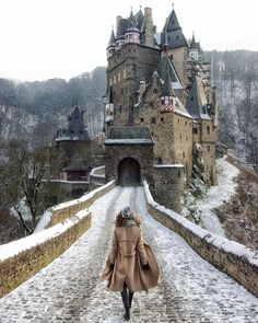 a woman walking down a cobblestone road in front of a castle with snow on the ground