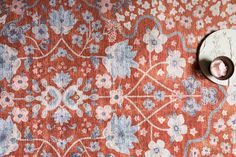 an orange and blue floral rug with a button on the ground next to it,