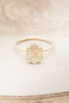 a gold ring with a rough diamond on it sitting on a wooden surface, close up