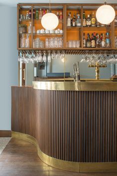 a bar with lots of bottles and glasses on the top shelf, along with lights above it