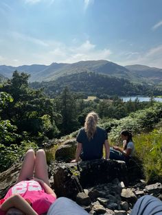 three people are sitting on rocks in the mountains looking at some water and hills behind them